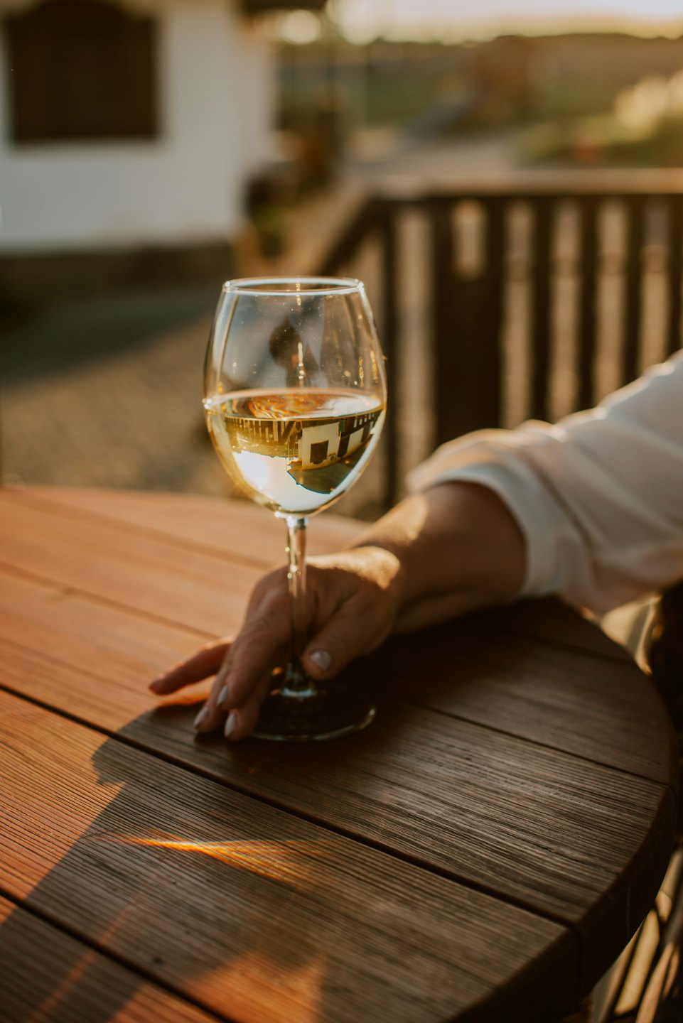 Mano che tiene un bicchiere di vino bianco su un tavolo di legno al tramonto.