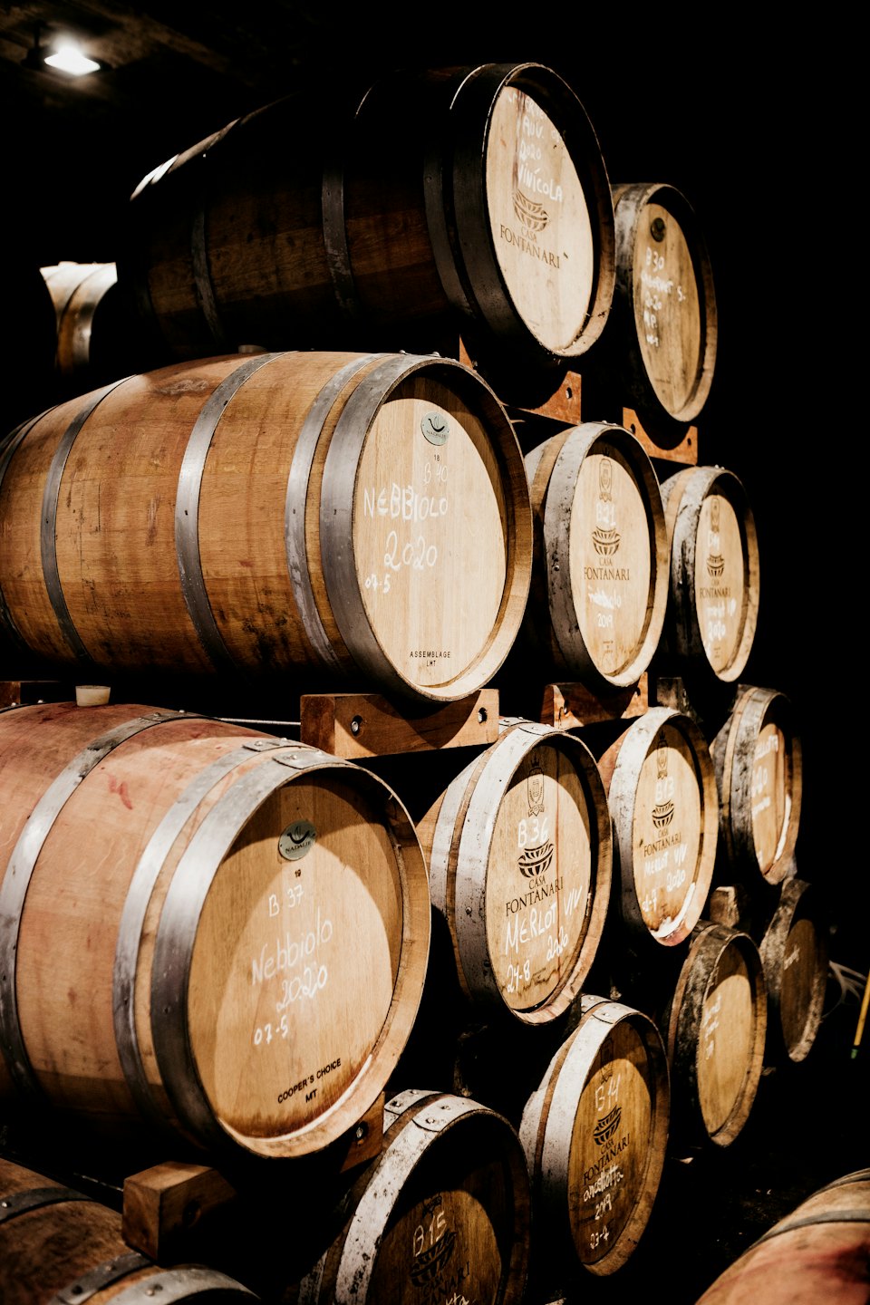 Botti di vino in legno impilate su rastrelliere in una cantina con etichette a gesso.